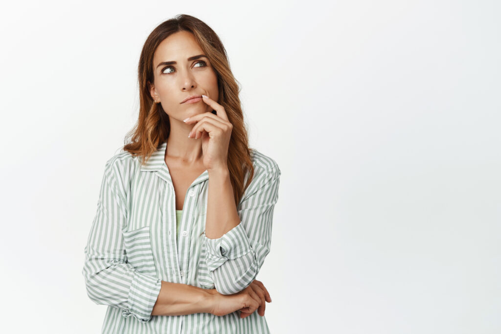 Image of thoughtful woman, wife thinking, looking up and touch lip, ponder important decision, making choice, standing in blouse against white background.