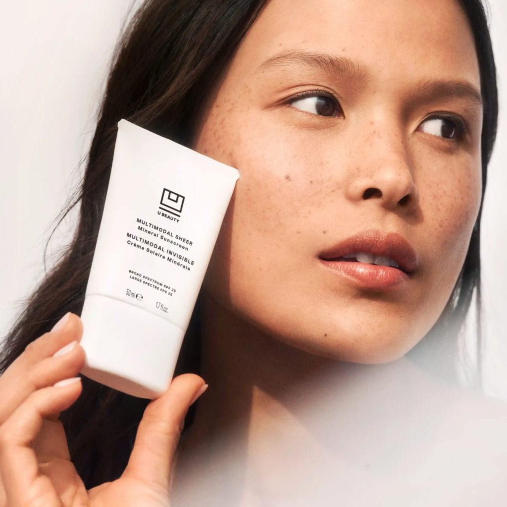 model holding sunscreen beside face